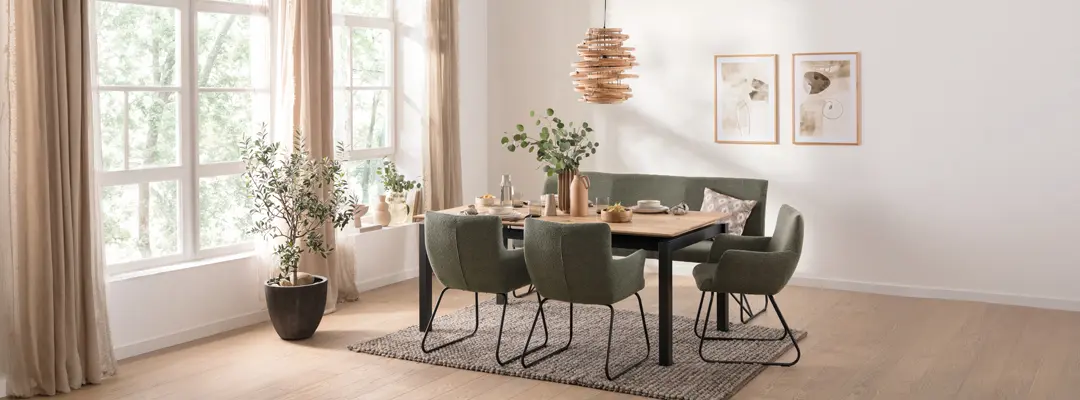 Holztisch mit sechs grünen Polsterstühlen, Teppich, Pflanzen und Bildern an der Wand